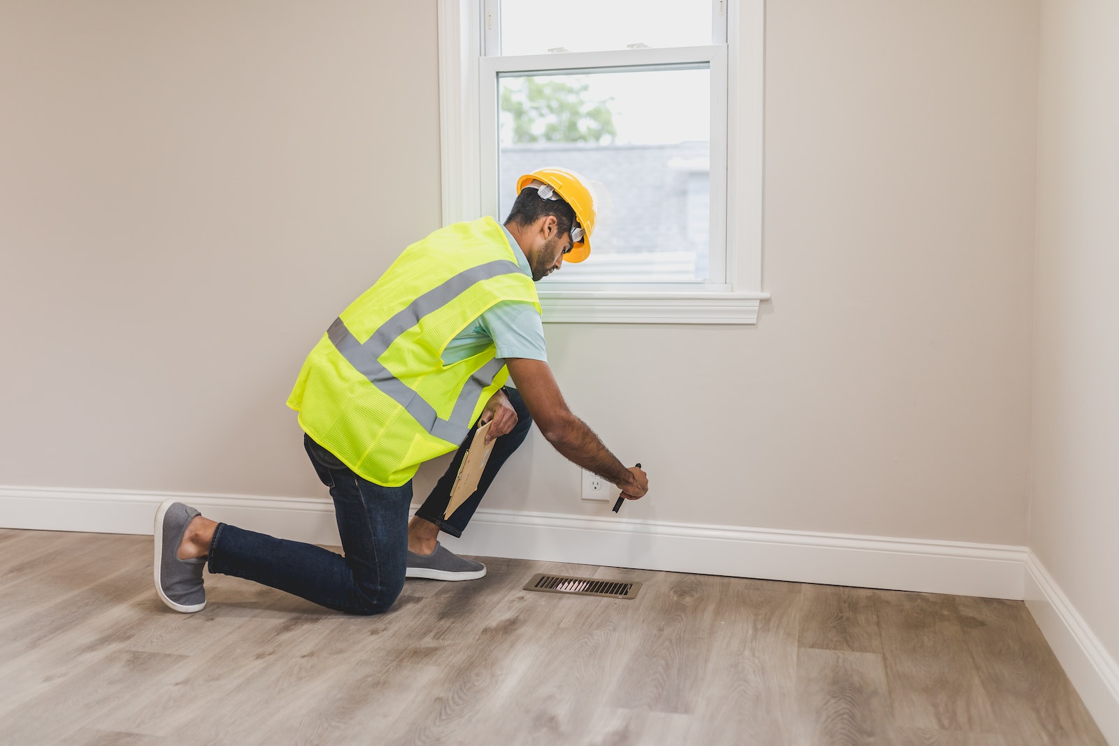 Man Wearing Yellow Safety Vest and Helmet Checking the Floor of a House