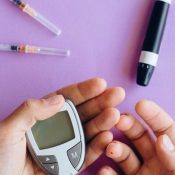 Person using a glucometer for a blood sugar test with insulin syringes on a purple background