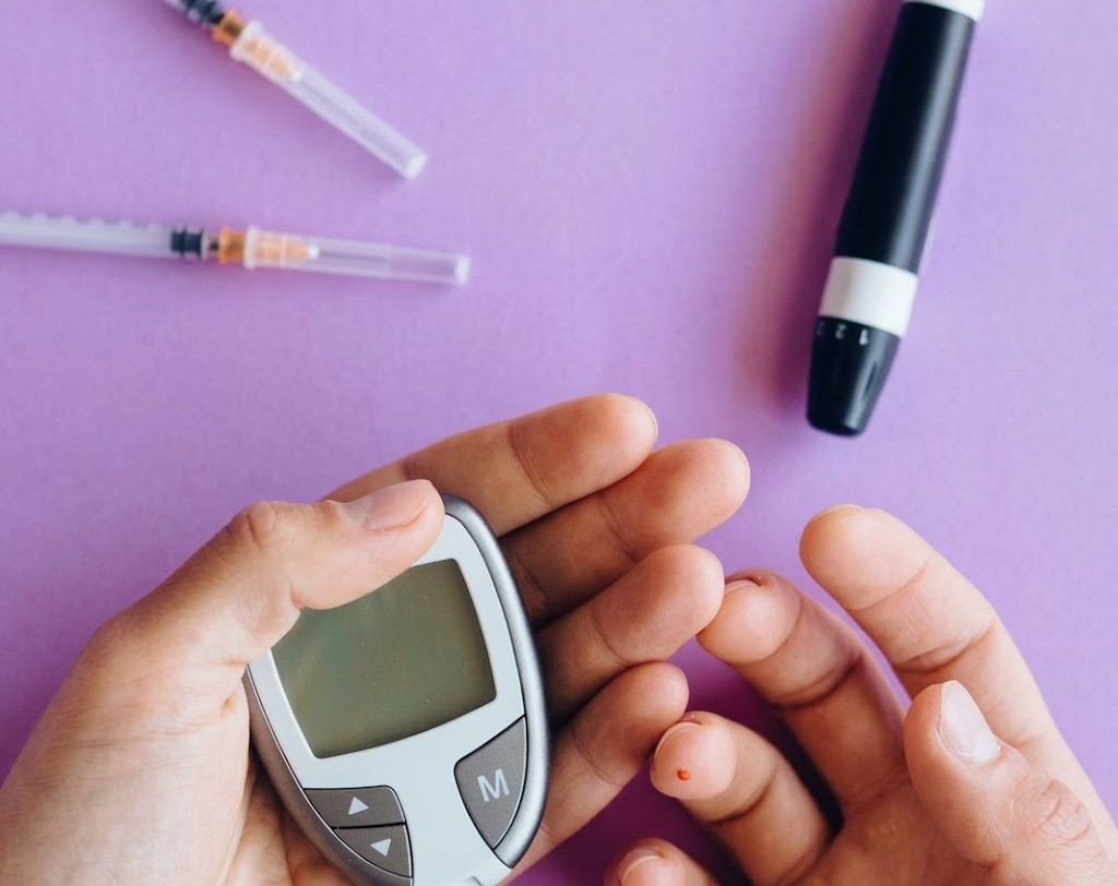 Person using a glucometer for a blood sugar test with insulin syringes on a purple background